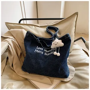 Detail of blue denim tote bag with white embroidery text and plush cloud charm accessory