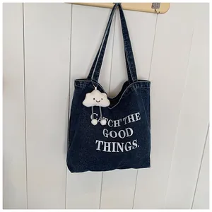Detail of blue denim tote bag with white text and cute cloud plush charm on strap