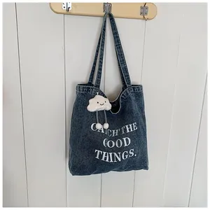 Detail of blue denim tote bag featuring white letter print and a cute plush cloud charm