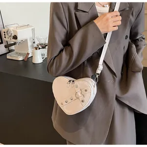 Vue détaillée d'un sac à bandoulière blanc en forme de cœur avec rivets sur un mannequin