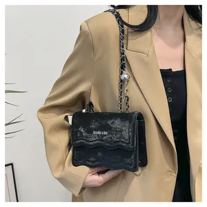 Détail du sac bandoulière noir avec bord ondulé et chaîne portée par un mannequin