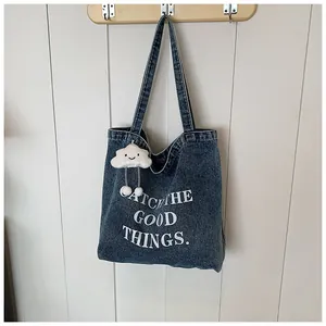Detail of dark blue denim tote bag featuring white printed text and a plush cloud charm
