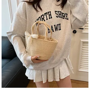Détail d'un sac cabas en paille tissée avec un nœud décoratif en dentelle blanche