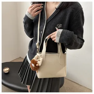 Close-up of cream white lychee texture bucket bag with a brown plush charm and strap