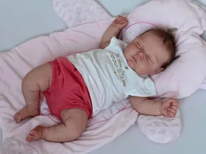 Detailed view of 50cm sleeping reborn doll in pink outfit on a soft plush animal cushion