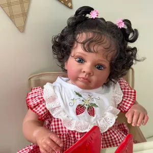 Muñeca reborn realista de 60cm con pelo rizado oscuro y babero de fresa en silla