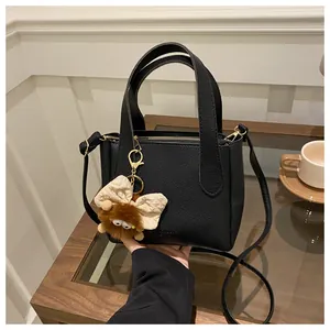 Detail of black pebbled leather bucket bag with top handles and cute plush charm on a table