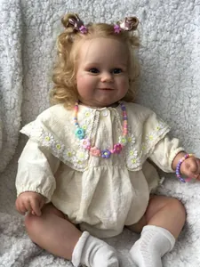 Détail de poupée reborn Maddie 60cm avec boucles blondes et broderie marguerite sur barboteuse