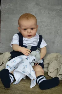 Realistic 60cm Sandie reborn doll boy in blue overalls holding a grey teddy bear toy