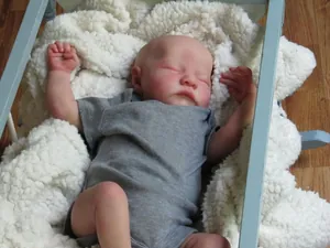 Realistic sleeping reborn baby doll in grey romper resting in a light blue wooden cradle