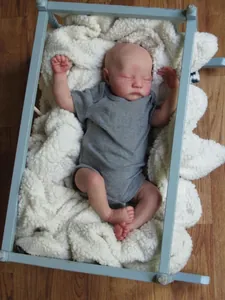 Lifelike reborn baby doll Levi sleeping in a blue wooden cradle with white blanket
