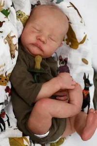 Close-up of sleeping reborn baby doll Levi with realistic skin texture and green outfit