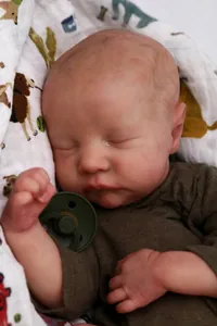 Close-up of sleeping reborn doll Levi with realistic skin texture and green pacifier