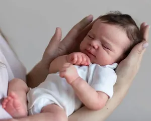 Detailed view of a 50cm sleeping reborn baby doll being held in hands on grey background