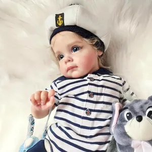 Realistic reborn toddler boy doll in navy sailor outfit with blue eyes on soft plush base