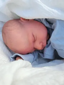 Close-up of a realistic reborn baby doll sleeping in a soft blue knit outfit and white wrap