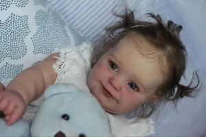 Detailed close-up of Maddie reborn doll in white lace dress with blue plush bear