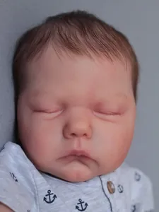 Close-up of sleeping reborn baby doll with realistic facial details and anchor print outfit