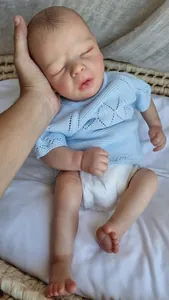 Close-up of a 16-inch lifelike reborn baby doll in blue knitwear sleeping in a basket