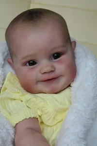 Nahaufnahme der 60 cm Reborn-Babypuppe mit braunen Augen und gelbem Rüschenoberteil