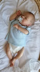 Detail of a lifelike 16 inch reborn baby doll in a blue knit top resting on white bedding
