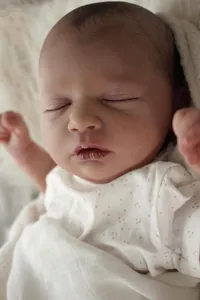Close-up of sleeping reborn baby doll face in white polka dot outfit and knit blanket