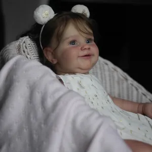 Poupée réaliste Maddie 60cm en robe blanche fleurie assise sur une chaise tressée
