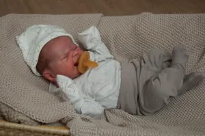 Close-up of lifelike newborn doll in gray outfit sleeping on beige blanket in woven basket
