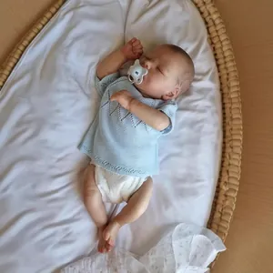 Lifelike 16-inch reborn baby doll sleeping in cradle wearing blue knit top with pacifier