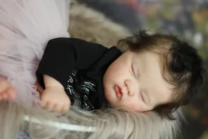Close-up of sleeping reborn baby doll with brown curly hair and pink tutu dress