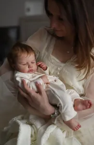 Close-up of realistic newborn reborn doll sleeping in woman's arms with detailed skin