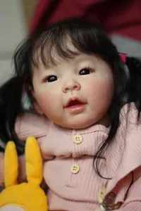 Close-up of realistic newborn doll with black pigtails and pink knit sweater details