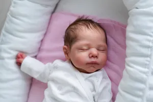 Close-up of sleeping reborn baby doll in white sheep print onesie on pink fabric
