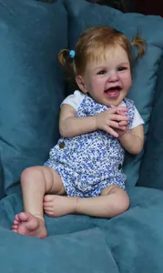 Gros plan détaillé d'une poupée reborn réaliste de 60cm avec un sourire et habit fleuri