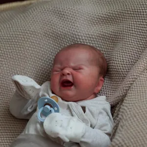 Lifelike 49cm reborn baby doll with realistic crying expression in white romper