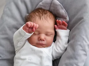 Close-up of sleeping 19-inch reborn baby doll in white sheep onesie on gray cushion
