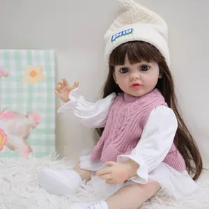 55cm levensechte Reborn babypop Betty met bruin haar en roze gebreid vest op tapijt
