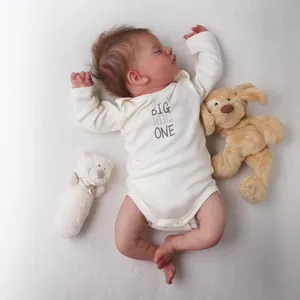 Lifelike 18-inch reborn baby doll in white onesie sleeping on a soft textured blanket
