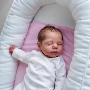 Lifelike 19-inch reborn baby doll sleeping in a pink blanket and portable white infant nest