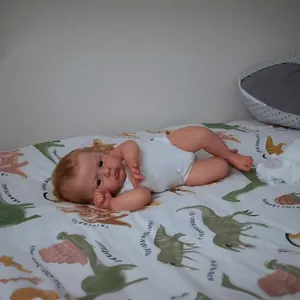 Realistic 24 inch reborn baby doll in white bodysuit on dinosaur print bedding