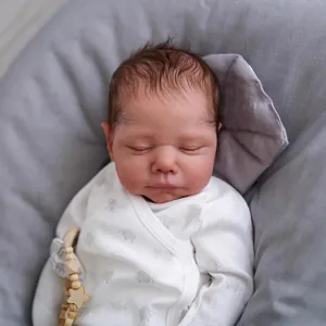 Realistic 19 inch reborn baby doll in white sheep print outfit on a soft grey bed