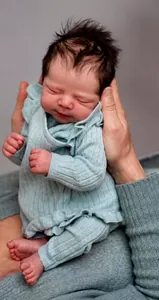 Close-up of 19-inch lifelike reborn baby doll in teal knit romper held by hands