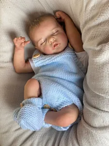 Detail of reborn baby doll in blue knit outfit with handmade wood buttons on white blanket