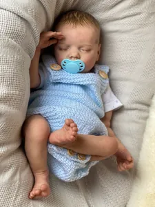 Close-up of sleeping reborn baby doll with lifelike skin texture and blue knitwear