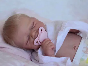 Detailed view of sleeping reborn doll with blonde hair and a pink pacifier accessory