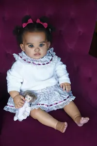 Gros plan détaillé d'une poupée reborn de 55cm en robe florale violette et pull tricoté