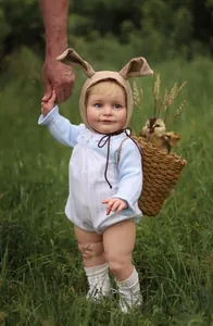Detail of 55cm baby doll wearing blue striped romper and bunny ear hat in outdoor setting
