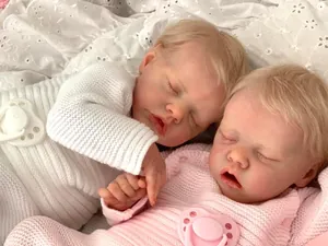 Close-up of 48cm twin reborn dolls in white and pink knit outfits on lace fabric