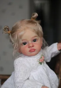 Gros plan d'une poupée reborn réaliste avec couettes blondes et robe en dentelle blanche