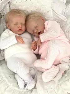 Close-up of sleeping twin reborn dolls in white and pink knit outfits on soft lace fabric